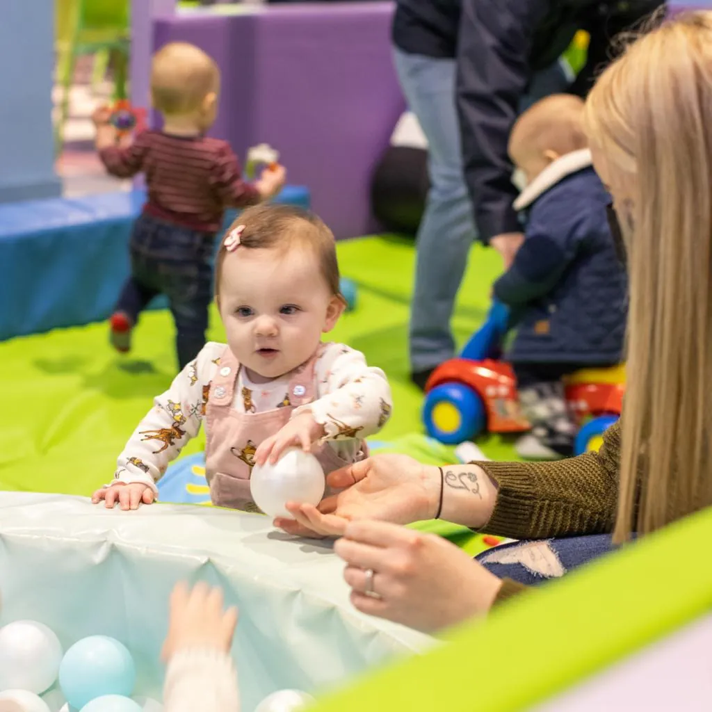 A baby sits in the ball pit of the toddler play zone at Fun Street while a parent watches