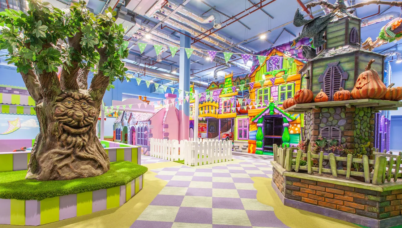 The storybook street at Fun Street soft play in Glasgow: a talking tree, painted playhouses and a chequered floor under bunting
